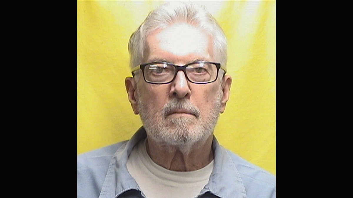 John Boyle wearing a blue shirt over a white shirt standing in front of a yellow background.