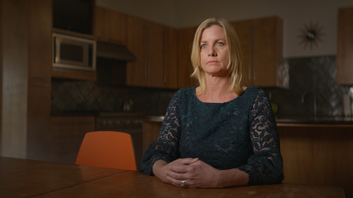Kim Byers sitting in front of a wooden desk looking serious.