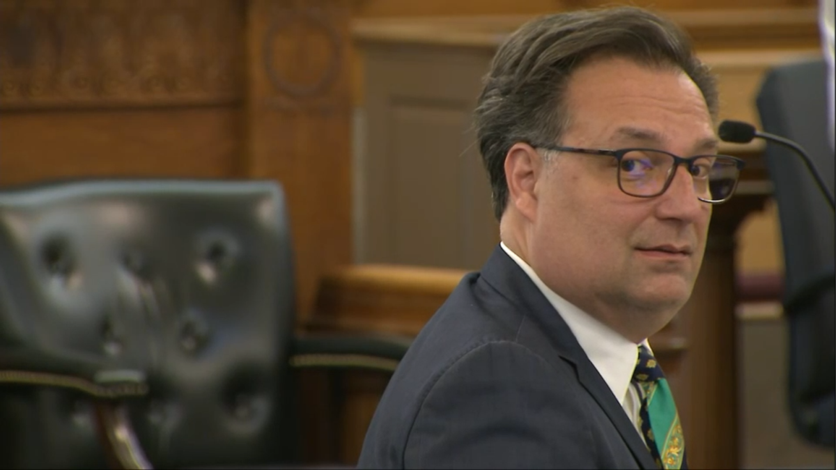 Brian Walshe looking over his shoulder in court. He is clean-shaved, wearing glasses and a dark suit with green tie.