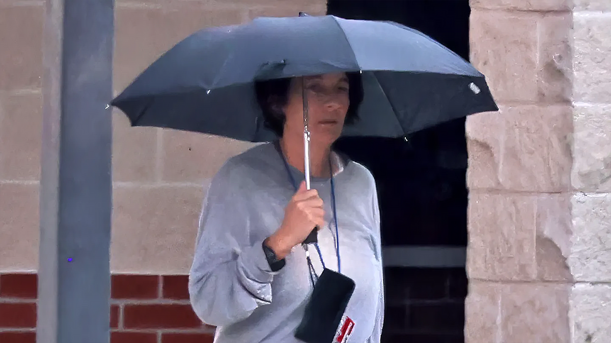 Ghislaine Maxwell in prison clothes carrying an umbrella in the yard