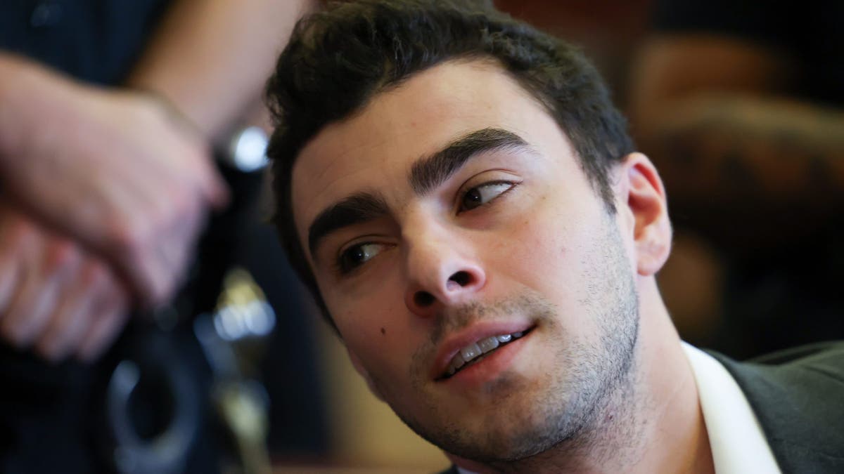 Luigi Mangione leans over in court with a 5 o-clock shadow