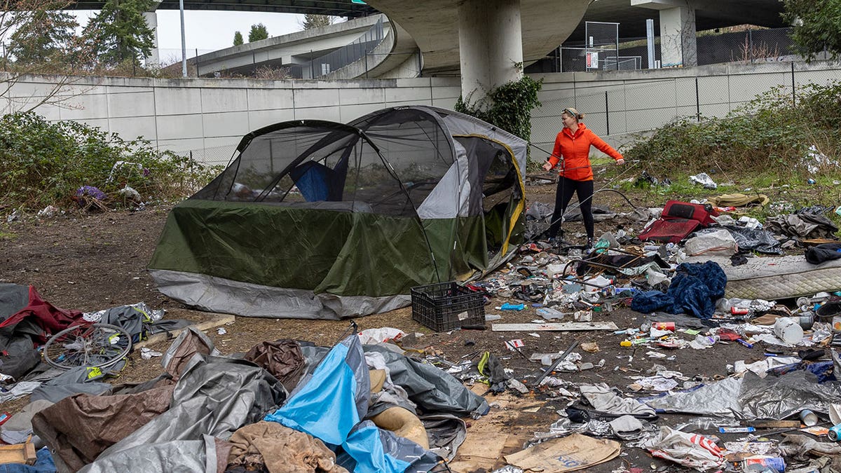 Woman clears debris from a homeless encampment beneath a highway overpass