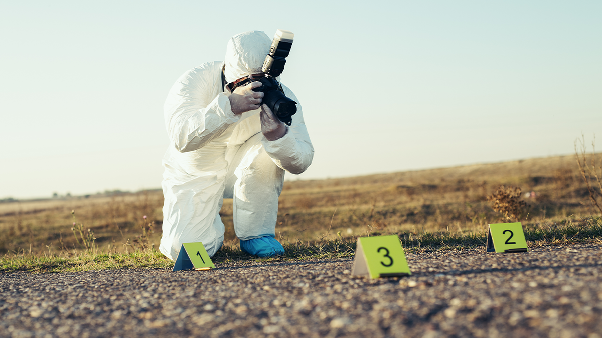 A forensic investigator in a full protective suit photographs evidence at a crime scene