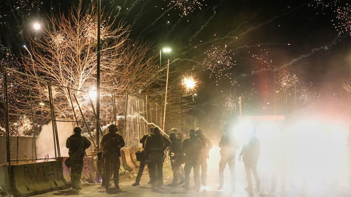 Fireworks explode above federal agents during a protest outside a Minneapolis federal building at night.