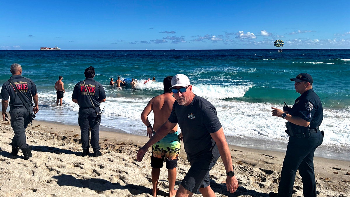 beachgoers and rescuers swim out to rescue paraglider