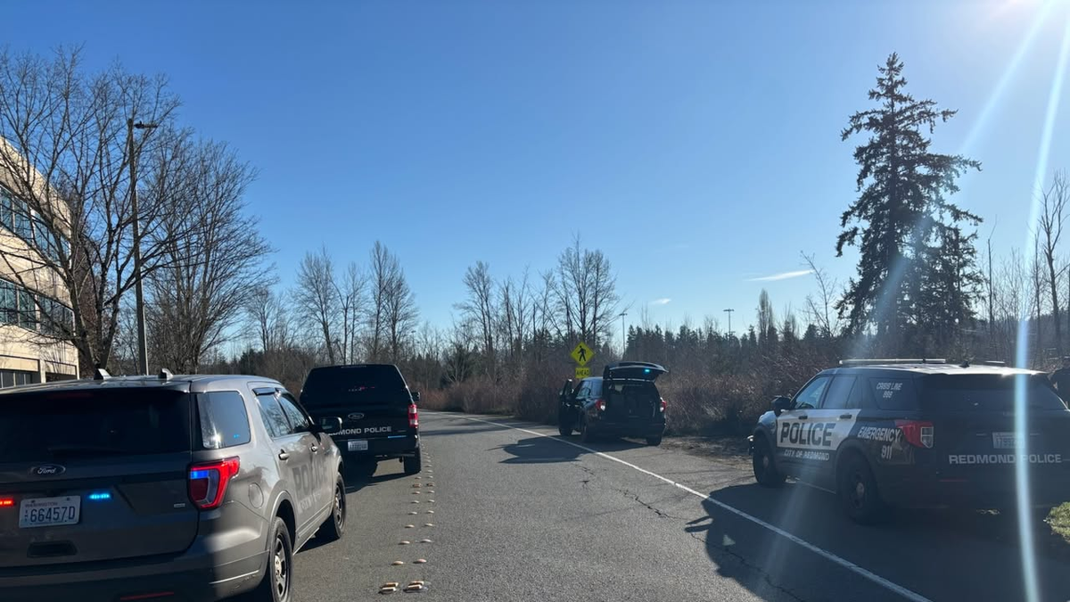 Police vehicles block a roadway near a wooded trail in Redmond