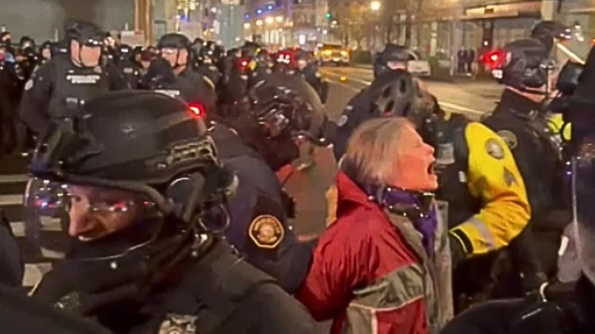 A protester shouts as police in riot gear form a line during a nighttime ICE protest in Portland.