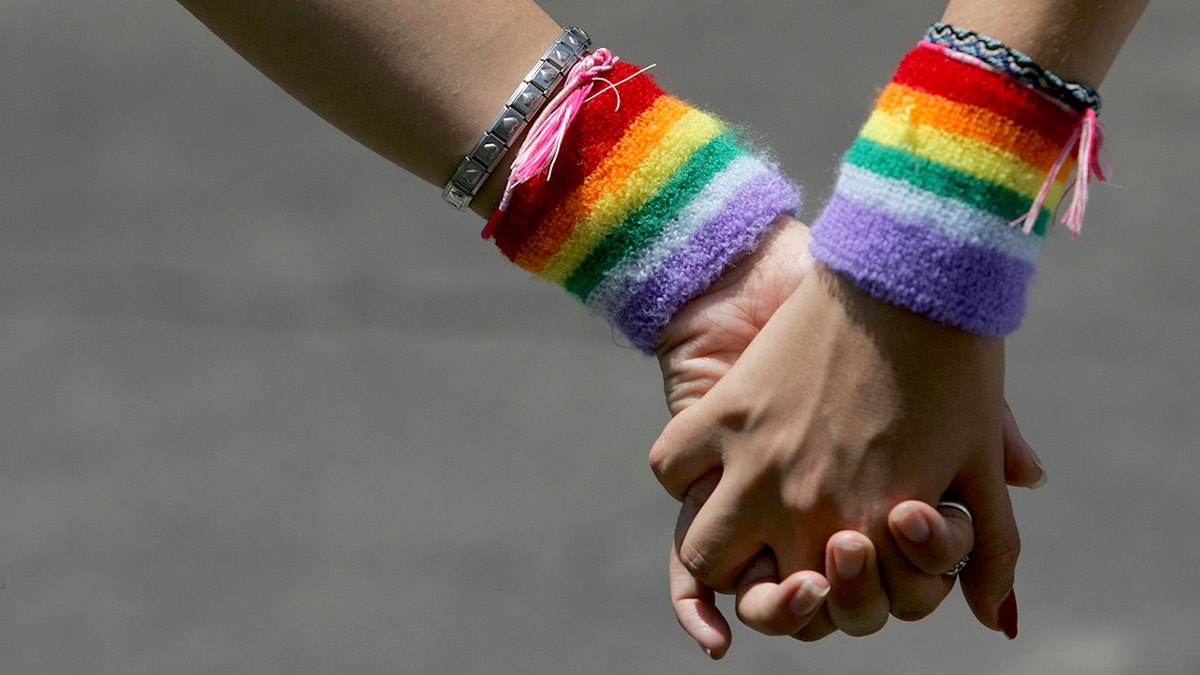 People hold hands while wearing rainbow-colored wrist bands