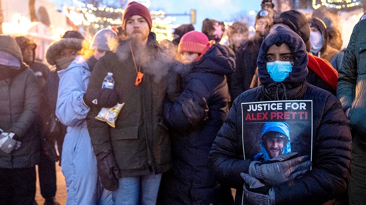 People stand with signs at a makeshift memorial where a man was fatally shot.
