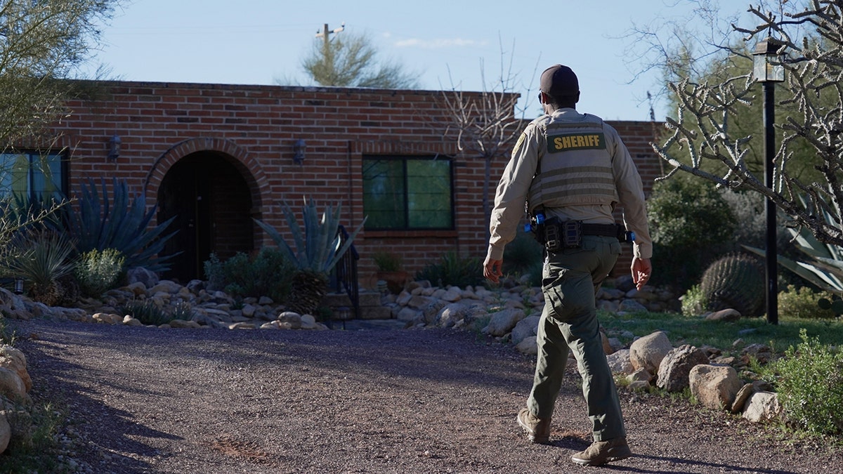 A member of the Pima County Sheriff's office standing on a residential street near Nancy Guthrie's house.