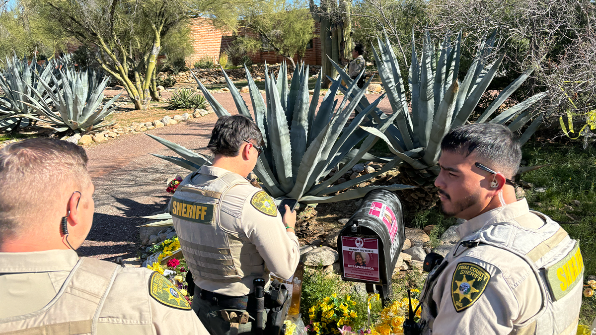 Three Pima Deputies examine a flyer taped to the mailbox outside Nancy Guthrie's home in Tucson