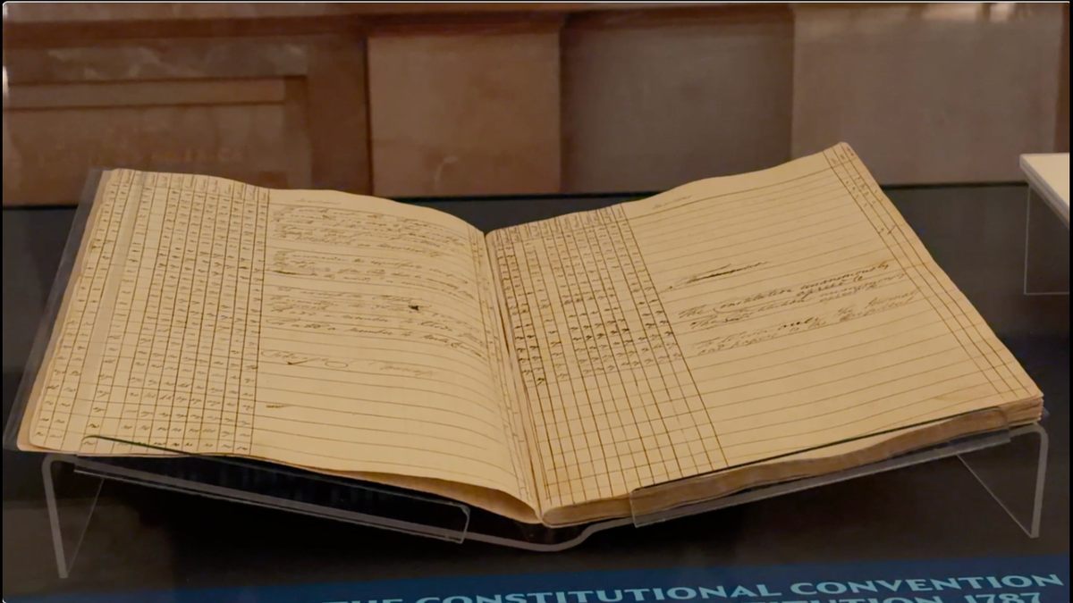 Historic ledger showing a tally of votes approving the U.S. Constitution in 1787 displayed in a museum exhibit.