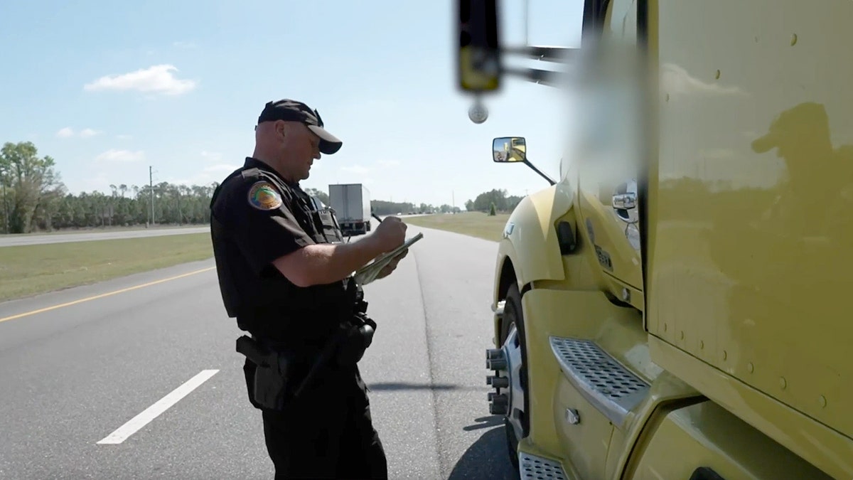 State trooper writing in a notebook beside a truck