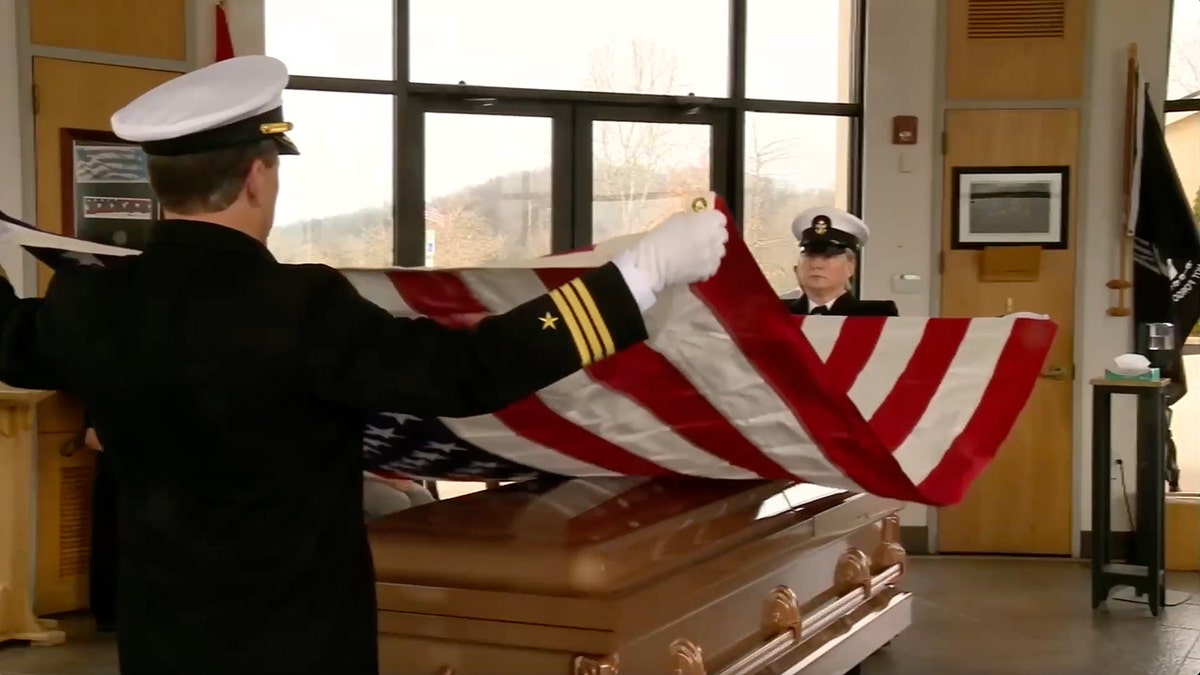 Two Naval officials hold American flag over casket