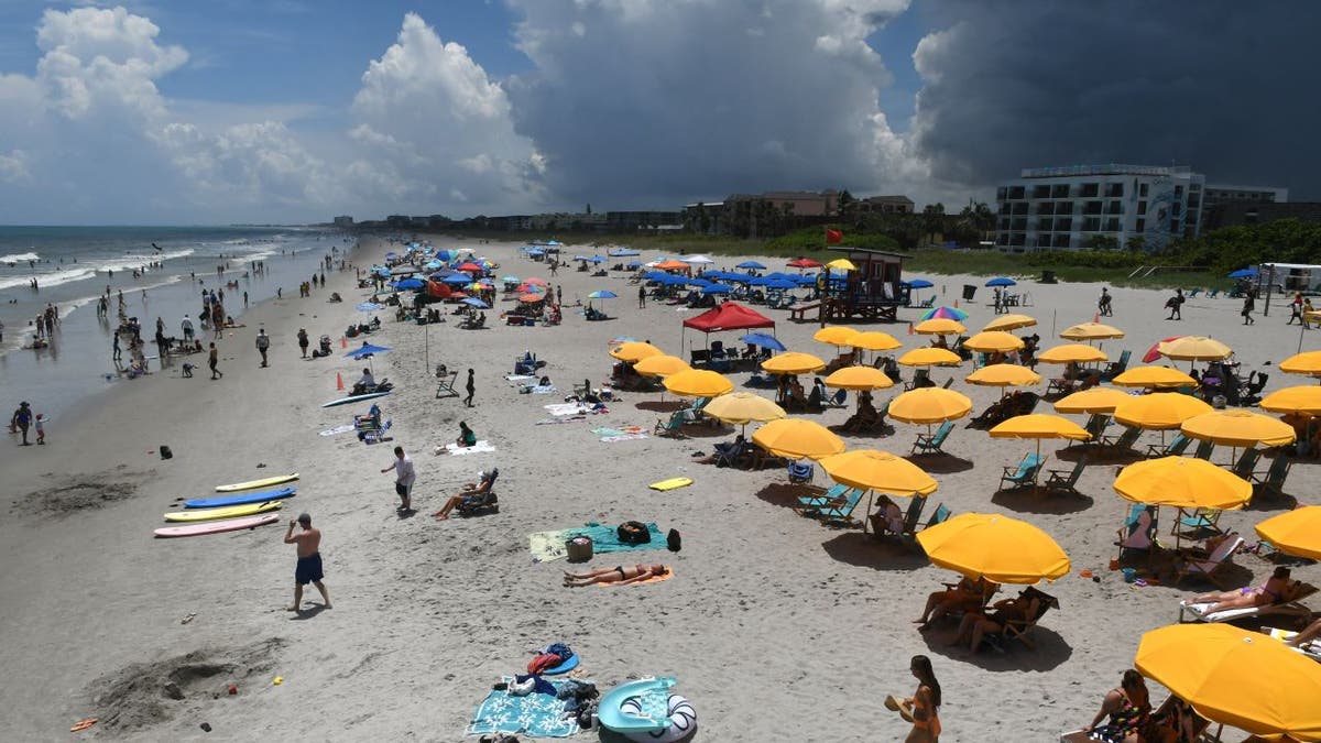 Beachgoers sitting and standing on Cocoa Beach with umbrellas