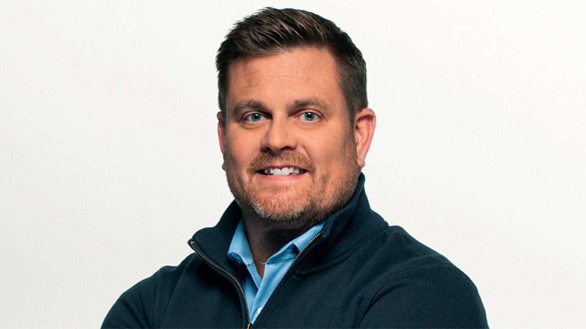 Brian Thompson smiling in a blue button down shirt and blue zip-up jacket