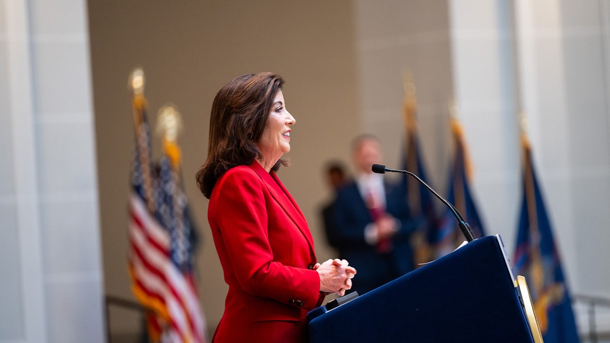 Governor Kathy Hochul signing a document at a desk in Brooklyn New York