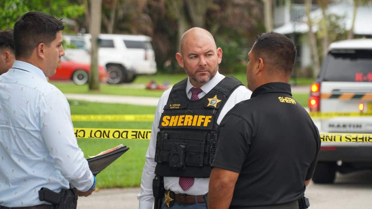 A man wearing a black shirt and blue jeans standing on a sidewalk near a building