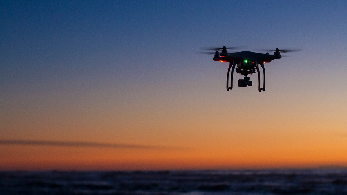 A drone flying over the ocean at dawn with a clear sky.