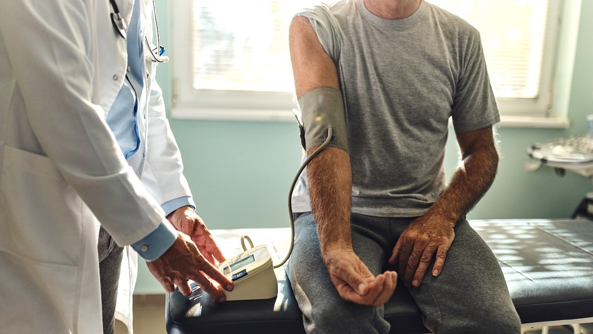 Male doctor measuring blood pressure of patient in hospital room