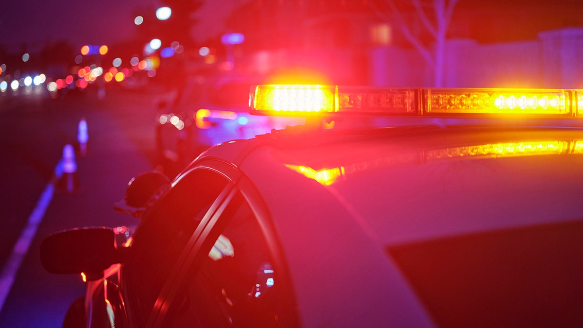 An Oklahoma man standing near a police car with red emergency lights on a road at night