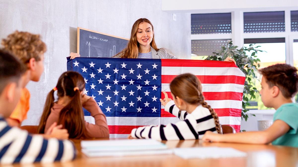 A teacher holding an American flag in a classroom with students