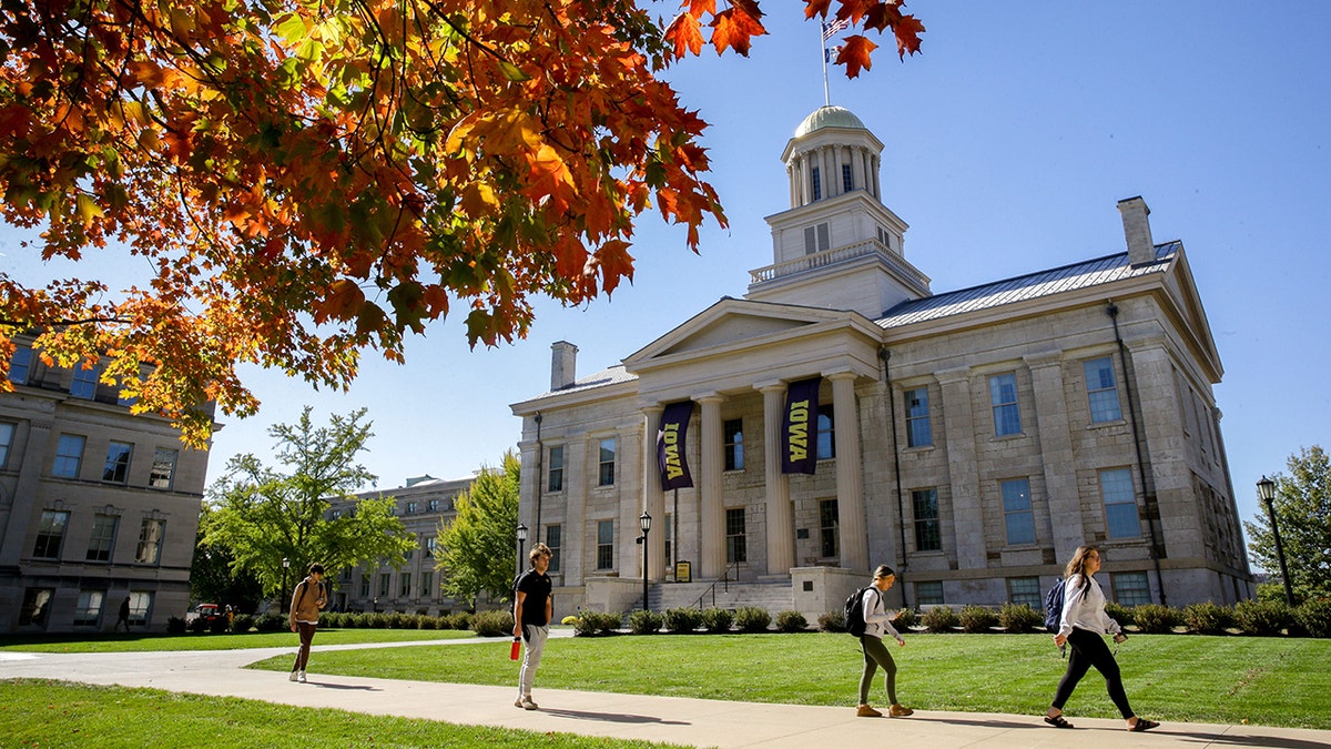 People walking past a tree with changing leaves near the Old Capitol building at University of Iowa campus