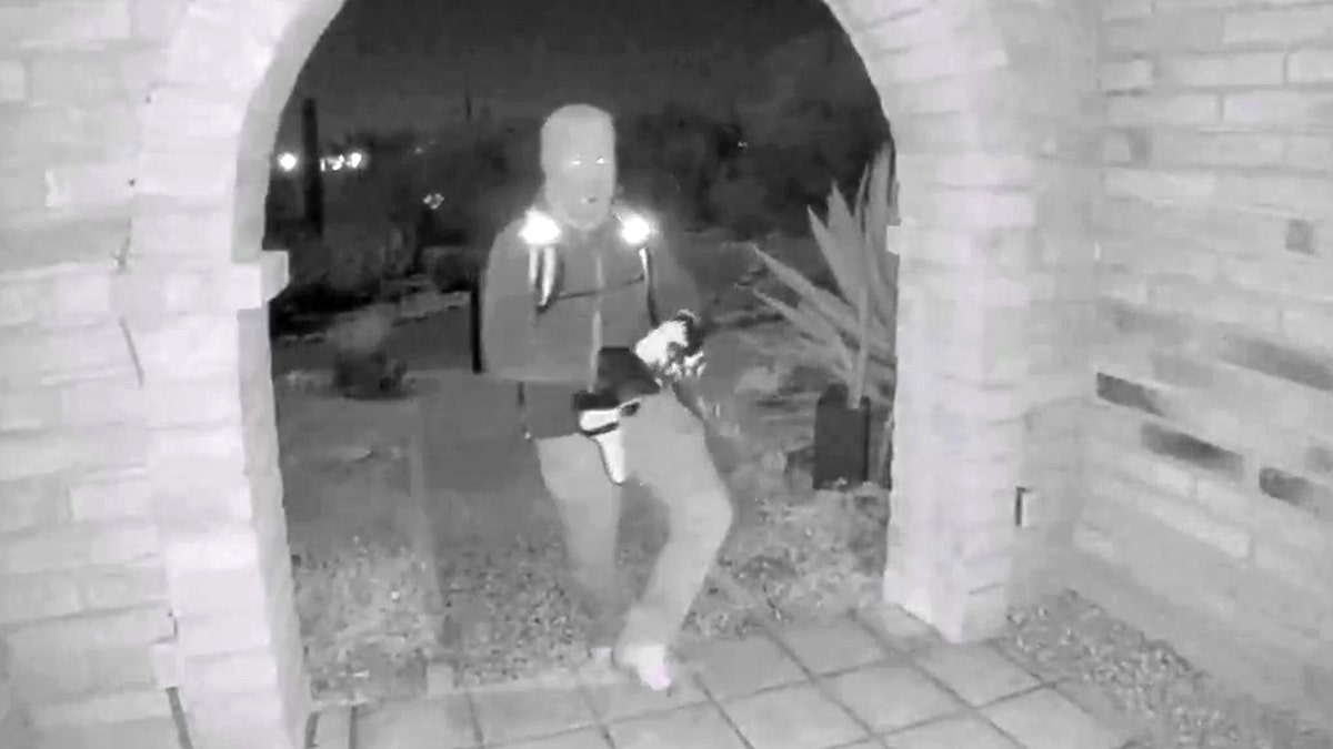 An armed individual reaching toward a Google Nest camera at Nancy Guthrie's front door in Tucson