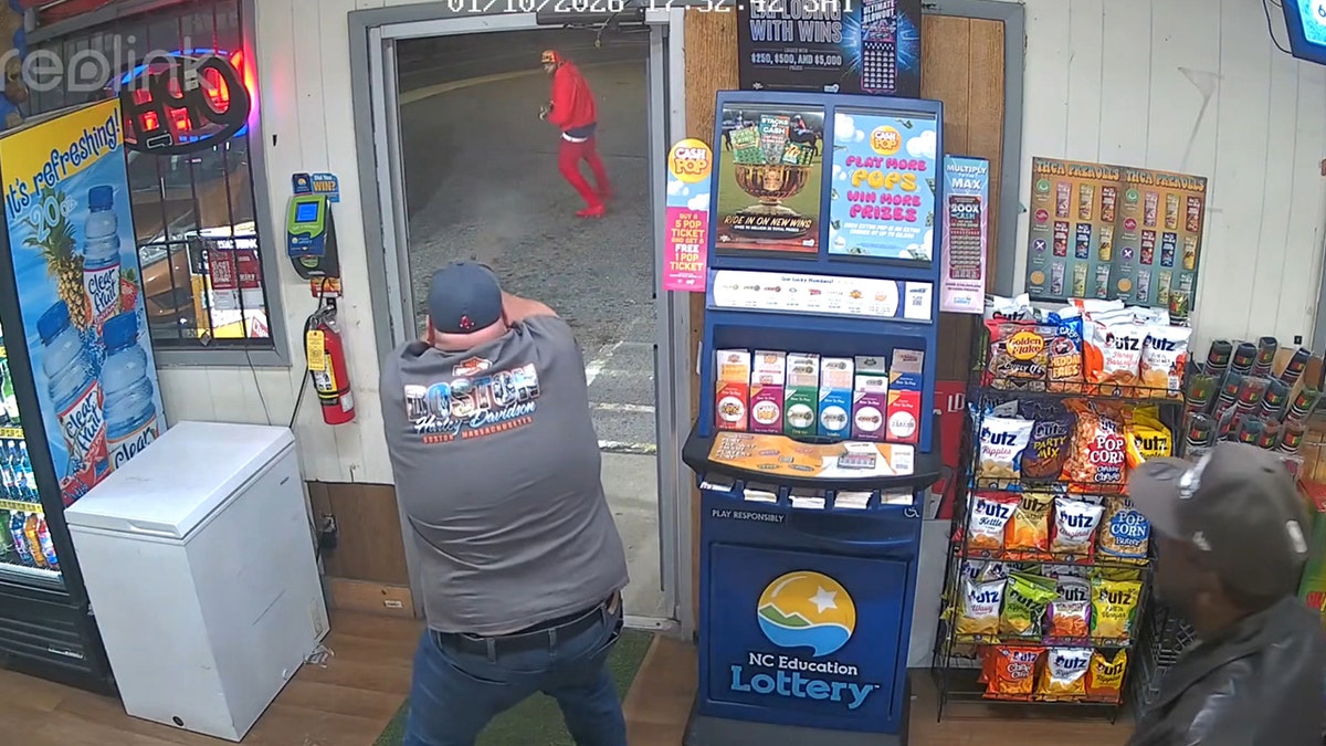 An officer wearing a ball cap and grey t-shirt while he points a gun at a suspect