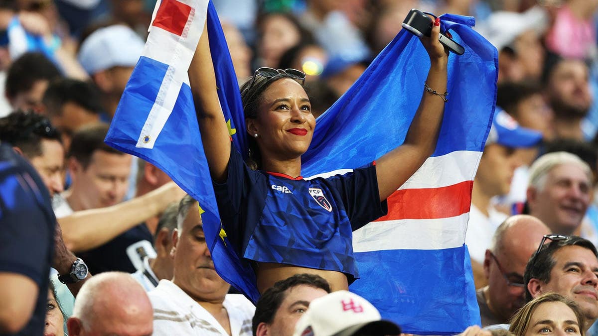 A Cape Verde fan wearing a team jersey and scarf at Miami Stadium during a World Cup match.