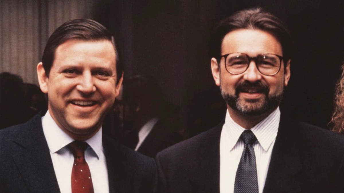 Jose Menendez and Peter Hoffman in matching dark suits at a business conference smiling.