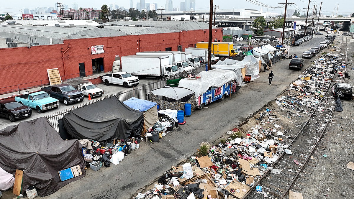 A person walking past large piles of trash inside a homeless encampment in downtown Los Angeles