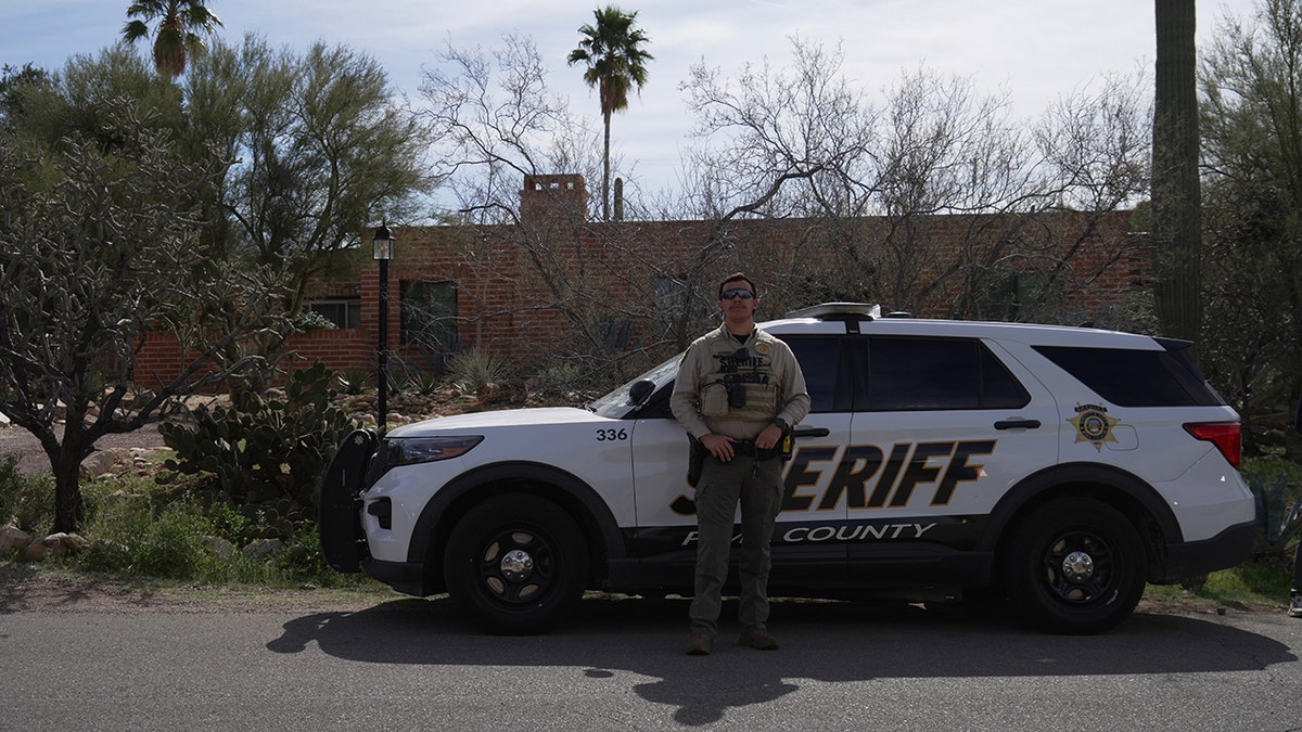 Pima County Sheriff's Department member standing next to vehicle outside Nancy Guthrie's home in Tucson