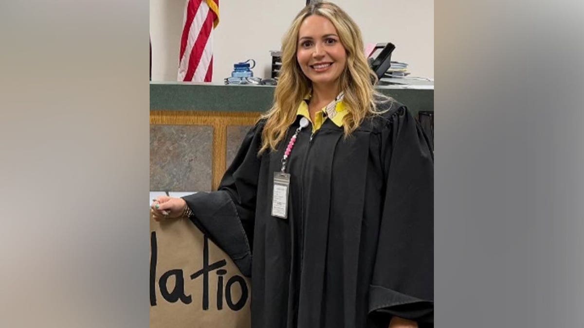 Judge Ashlee Cole stands in a black judicial robe in front of an American flag inside a courtroom office.