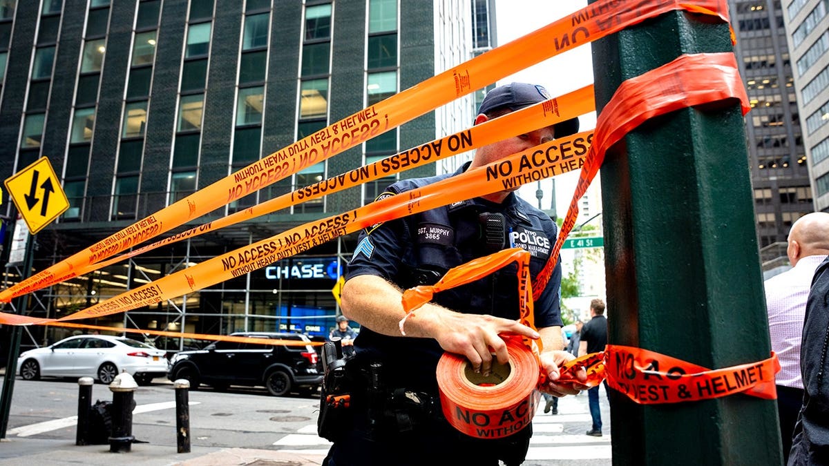 Police officer wrapping caution tape around pole and street