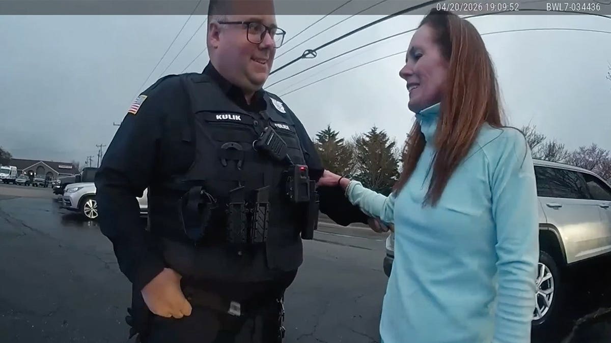 Bodycam still of police officer standing with woman in teal jacket in parking lot, timestamp visible on screen.