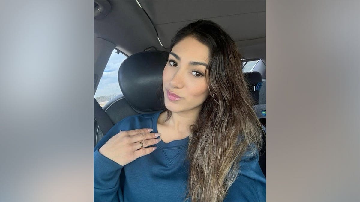 A woman in a blue sweatshirt takes a selfie in the driver's seat of a car.
