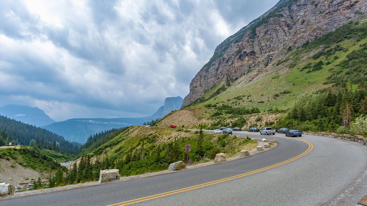 cars make a turn on a road alongside mountain