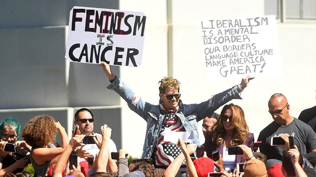 Conservative commentator Milo Yiannopoulos holds protest signs while speaking at the University of California in Berkeley, California, U.S., September 24, 2017. REUTERS/Noah Berger - RC1F9EBC0040
