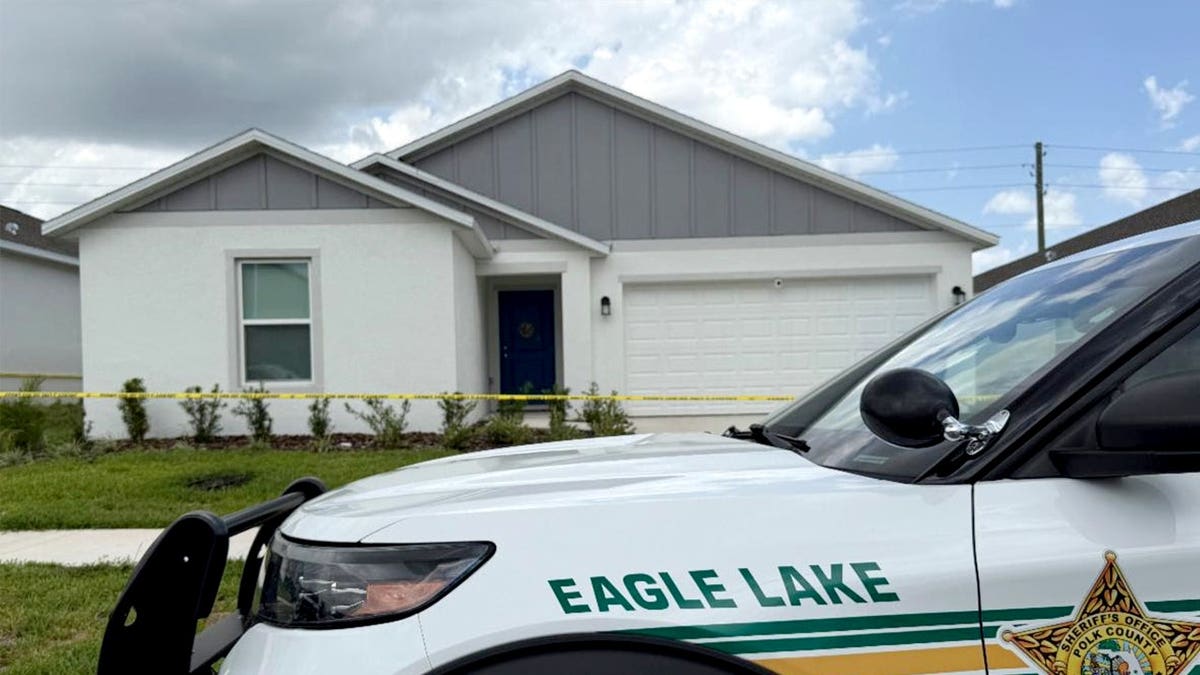 The exterior of a house is shown with a sheriff's car parked out front.