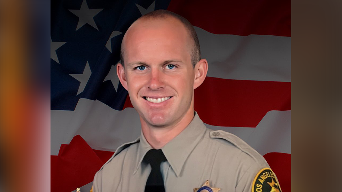 A portrait of Deputy Ryan Clinkunbroomer in his LASD uniform in front of an American flag