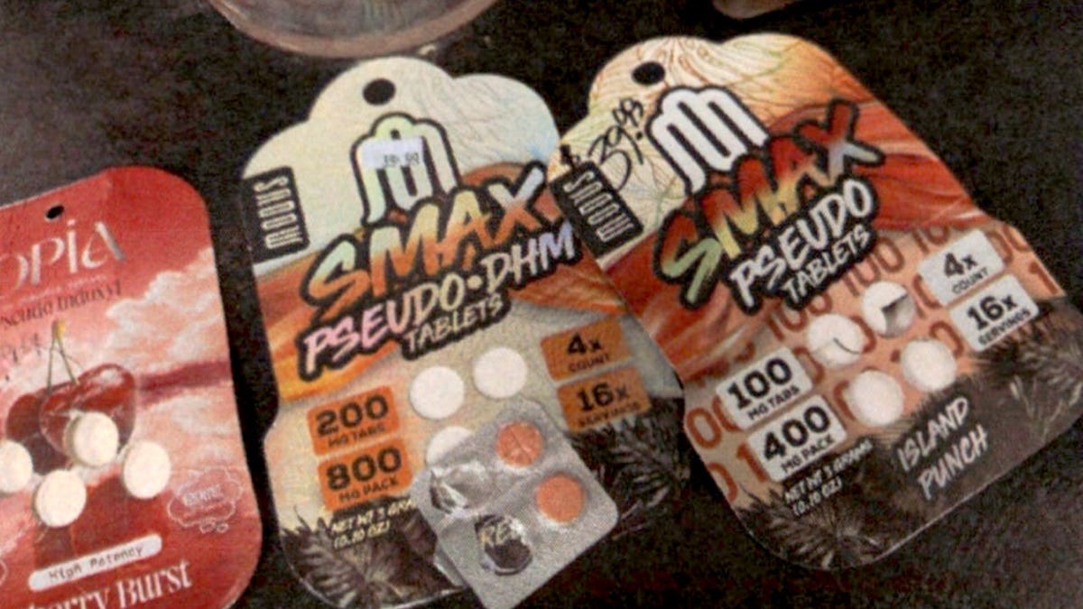 Three synthetic kratom tablet packages laid on a dark surface, including two Smax-brand packs and a cherry-flavored package, with loose tablets visible inside the blister packing.