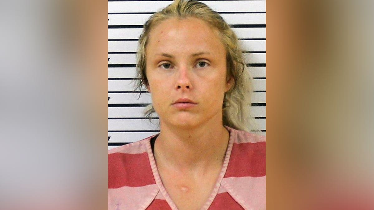 Booking photo of Geordyn Nichole Hayes, a blonde woman wearing a red-and-pink striped shirt in front of a height chart.