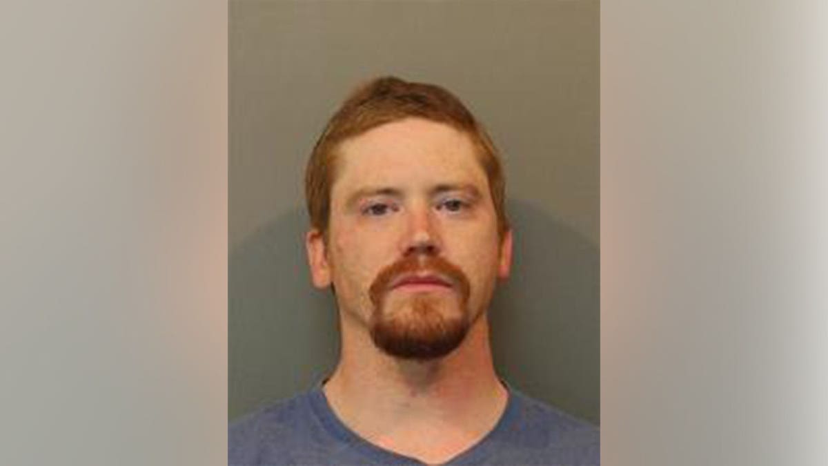 Mugshot of Eric Basco, a man with short reddish-brown hair and a beard, wearing a blue shirt against a gray background.
