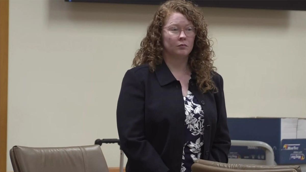 Caylen Deller stands in a Florida courtroom wearing glasses, a dark blazer and a floral blouse during proceedings in her boyfriend's murder case.