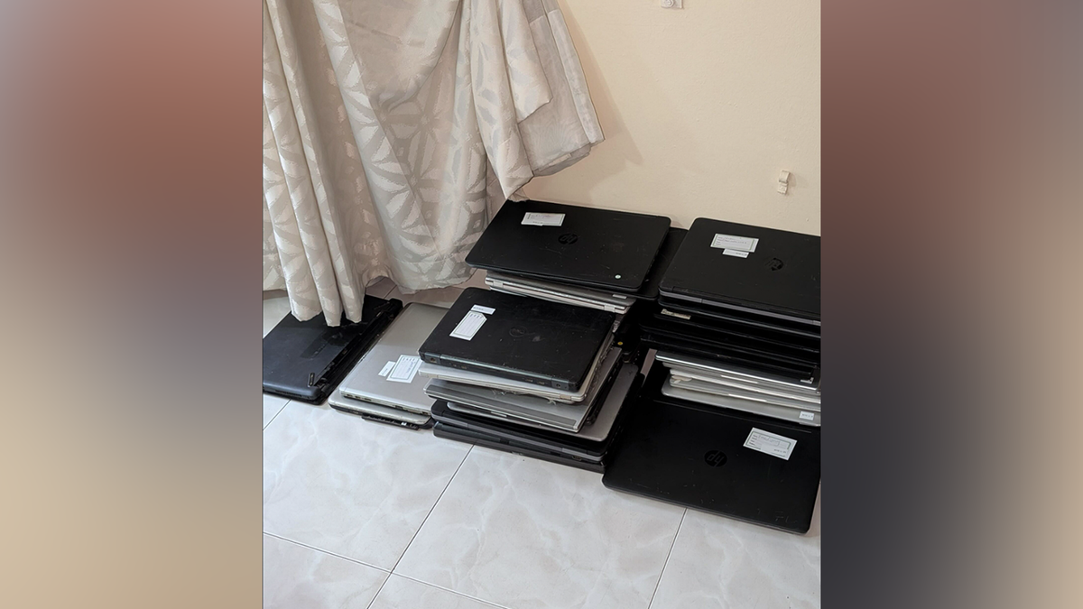 Stacks of laptop computers with evidence labels photographed during a scam center investigation in Ghana