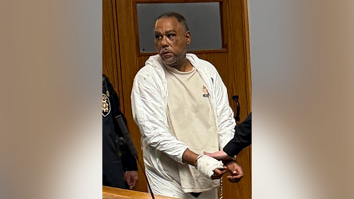 Nelson Blanco stands in court wearing white protective clothing with a bandaged hand